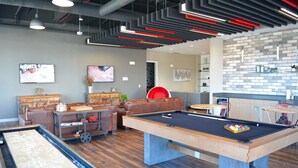 Una mesa de billar en un ambiente interior moderno, con suelo de madera, una silla roja y un porta billares.
