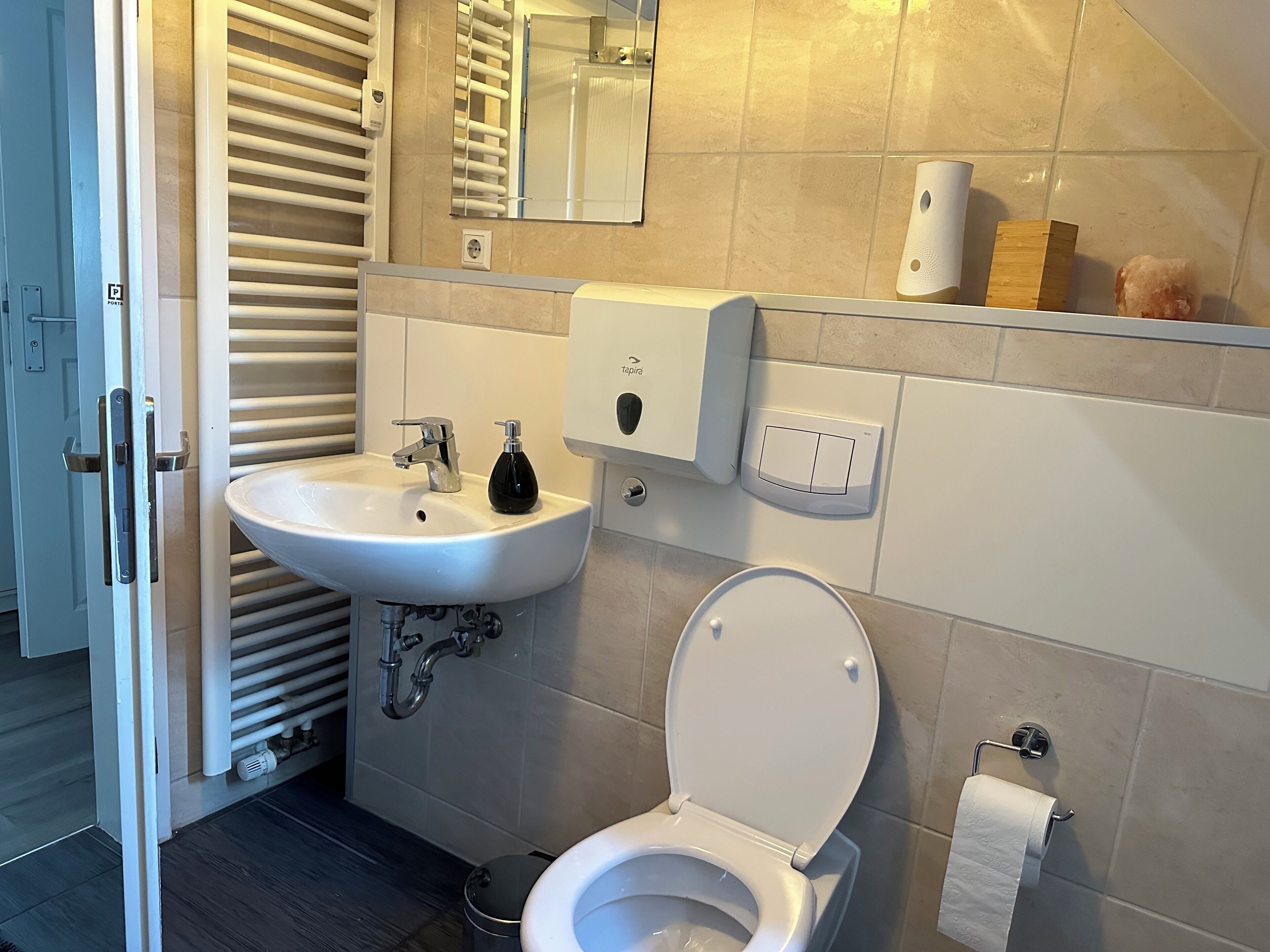 A bathroom with a sink, toilet, and towel dispenser.