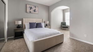 A bedroom with a large bed, two bedside tables with lamps, a chair, and a painting on the wall.