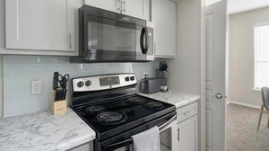 Une cuisine avec des meubles blancs, une cuisinière noire, un four à micro-ondes et un grille-pain.