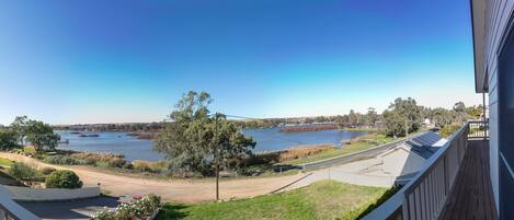 A balcony with a view of a lake, a road, and a bridge in the distance.
