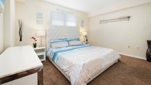 A bedroom with a large bed, a bedside table, a nightstand, a lamp, and a wall-mounted shelf. - Beachfront Condo w/ Pool & Balcony Sunset Views (Clearwater)