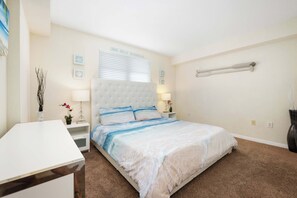 A bedroom with a large bed, a bedside table, a nightstand, a lamp, and a wall-mounted shelf. - Beachfront Condo w/ Pool & Balcony Sunset Views (Clearwater)