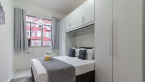 A bedroom with a bed, a wardrobe, a window with curtains, and a patterned rug. - Comfort 6 Minutes From Copacabana Beach Br801 (Rio de Janeiro)