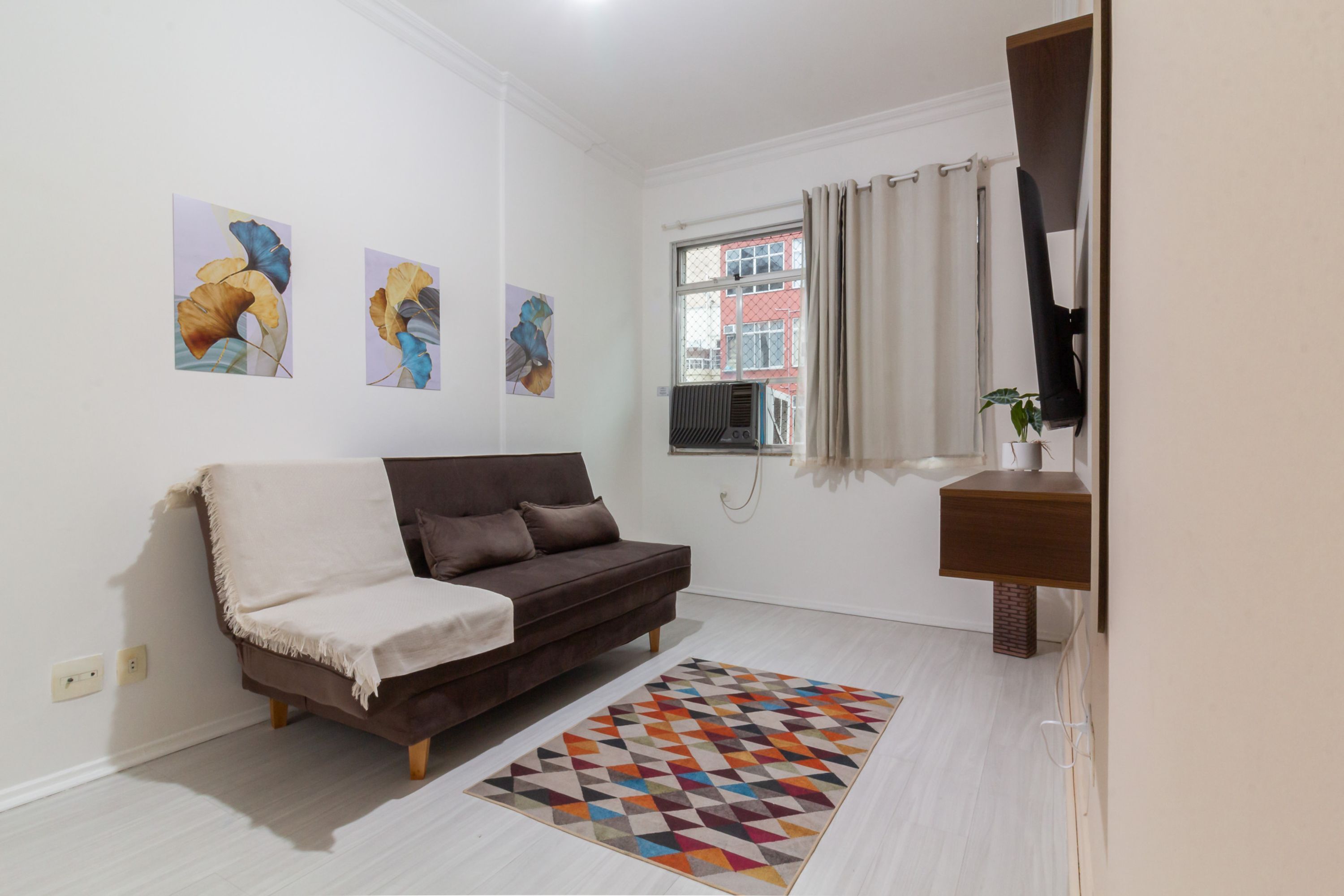 Un salon moderne avec un canapé marron, un tapis géométrique aux couleurs vives et des œuvres d’art accrochées aux murs.