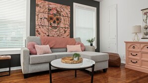 A living room with a grey sofa, a round coffee table, a large floral artwork, and a wooden floor. - Gothic Girl Stylish Upstairs Nook Near Shops & A&M (Bryan)