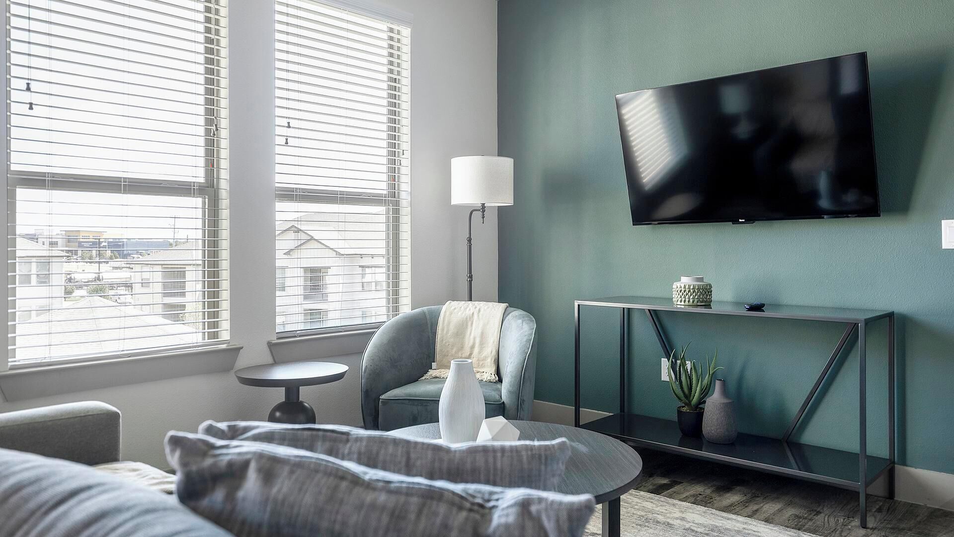 Een moderne woonkamer met een bank, een salontafel, een aan de muur bevestigde televisie en een vloerlamp.