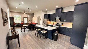 Una cocina moderna con armarios oscuros, una isla central y un comedor con sillas de madera y un cojín rojo.