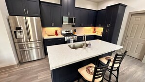 Una cocina moderna con gabinetes oscuros, electrodomésticos de acero inoxidable, encimera de granito y una isla integrada con taburetes de bar.