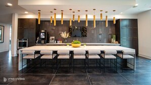 A modern kitchen with a large island, dark cabinetry, and pendant lighting. - Landing | Chic 1BD, Gym, Clubhouse (San Antonio)