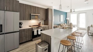 A modern kitchen with a large island, stainless steel appliances, and a bar area with stools. - Landing | Chic 1BD, Gym, Clubhouse (San Antonio)