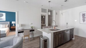 A modern kitchen with a central island, a dining area with a chair and table, and a bedroom with a bed and nightstand. - Landing | Chic 2BD, Pool, Clubhouse (San Antonio)