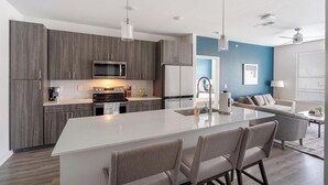 A modern kitchen with dark wood cabinets, stainless steel appliances, and a large island with seating. - Landing | Chic 2BD, Pool, Clubhouse (San Antonio)