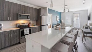 A modern kitchen with grey cabinets, stainless steel appliances, and a large island with bar stools. - Landing | Chic 2BD, Pool, Clubhouse (San Antonio)