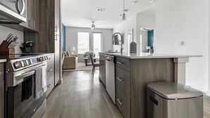 A modern kitchen with a built-in oven, a dishwasher, and a sink. There is a dining area with a table and chairs.