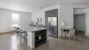 A modern kitchen with a central island, bar stools, a refrigerator, and a dining area with a table and chairs.