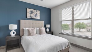 A bedroom with a large bed, two bedside tables, a headboard, a window with blinds, and a wall-mounted artwork. - Landing | Chic 2BD, Pool, Gym (McKinney)