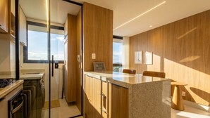 Una cuina moderna amb una porta de vidre, armaris de fusta, una encimera de granat i una zona de menjador amb taula i cadires.