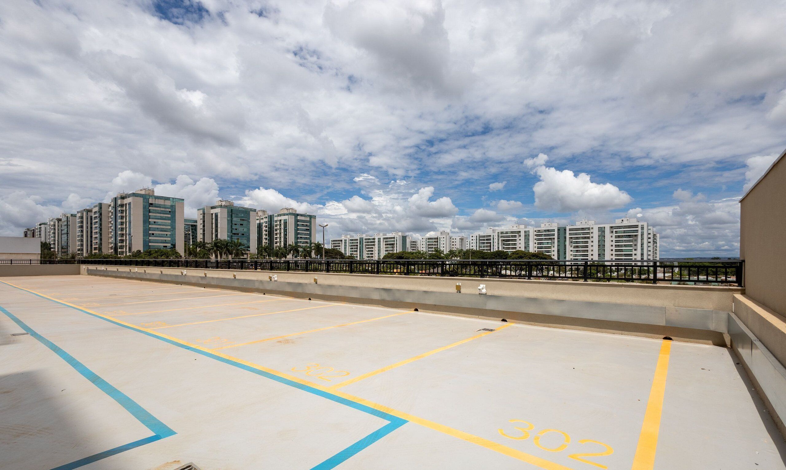 A rooftop parking area with marked spaces, a clear view of high-rise buildings, and a partly cloudy sky.