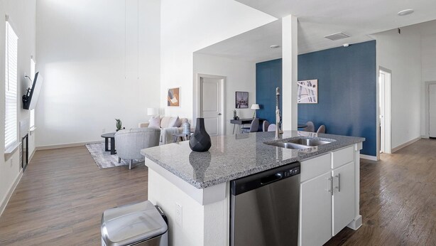 A modern kitchen with a central island, stainless steel appliances, and a blue accent wall. - Landing | Modern 3BD, Gym, Pool (Waller)