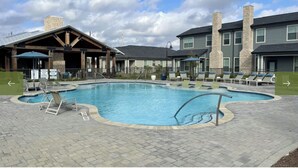 A swimming pool with lounge chairs and a covered area with a stone chimney. - Landing | Modern 3BD, Gym, Pool (Waller)
