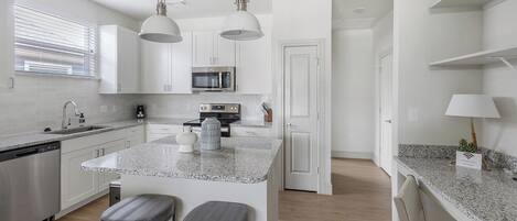 A modern kitchen with white cabinets, a granite countertop, stainless steel appliances, and pendant lighting.