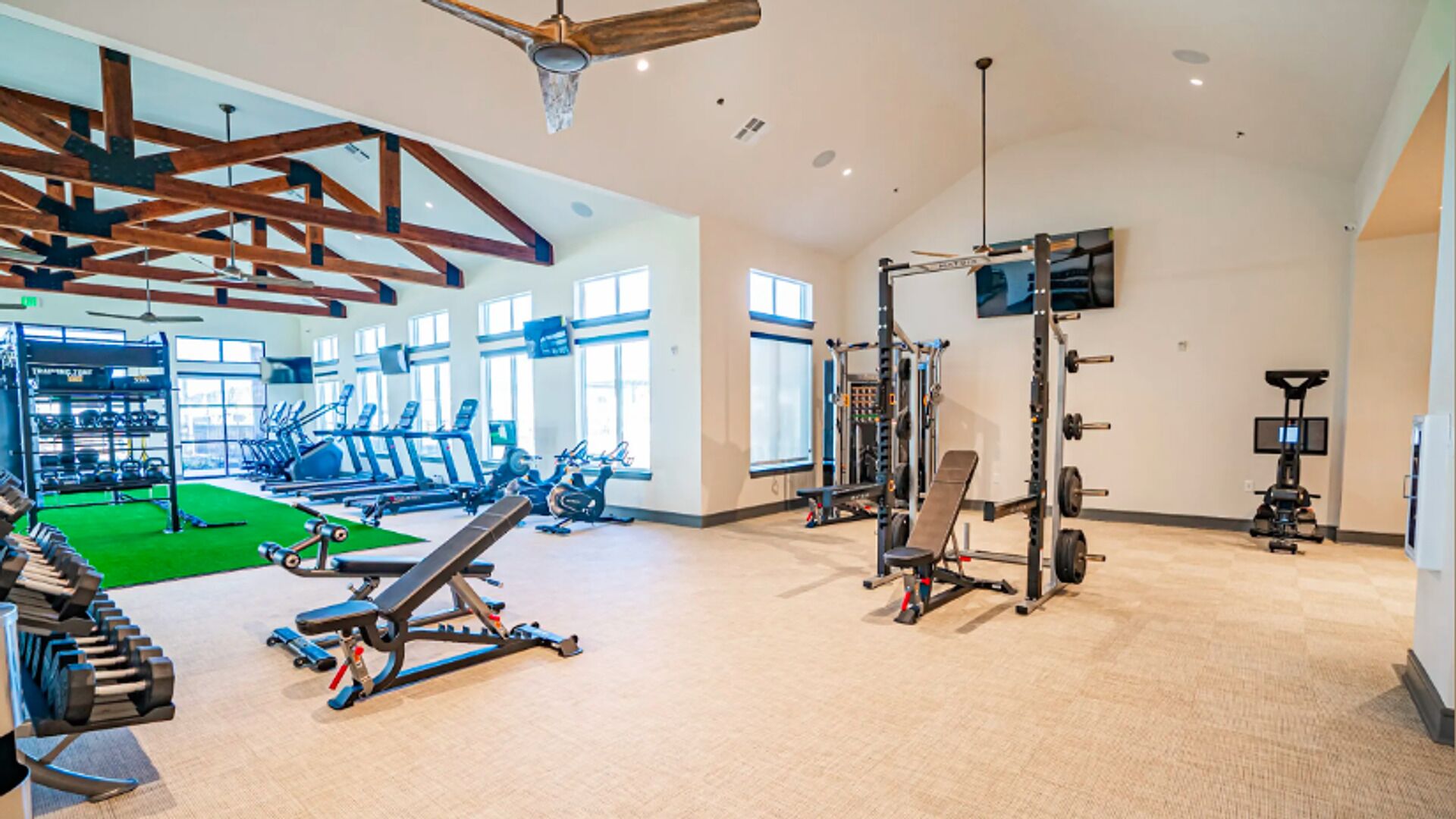 A spacious gym with various exercise equipment, large windows, and a high ceiling.