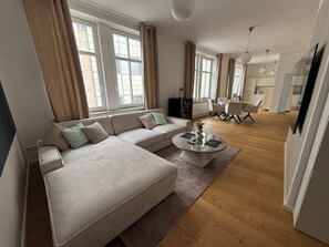 A modern living room with a large L-shaped sofa, a glass coffee table, and a dining area with a white table and chairs.