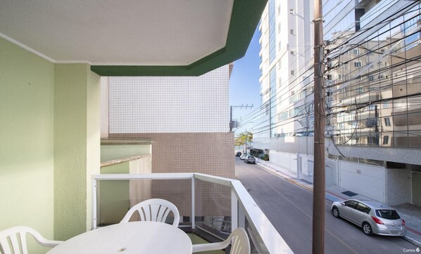 Un balcón con una mesa y sillas, con vista a una calle donde se ven coches aparcados y un edificio con fachada de tejas.