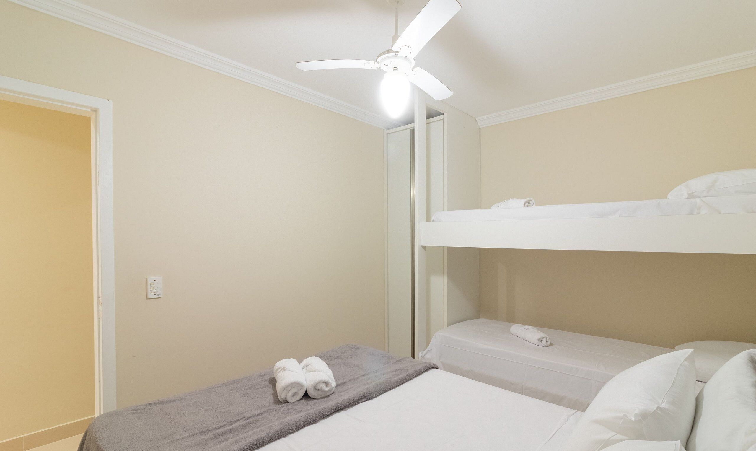 A small, single-bed room with a ceiling fan, a towel on the bed, and a mirror on the wall.