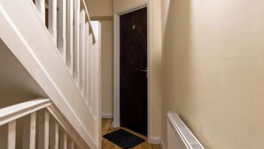 Un couloir étroit avec une porte sombre, des rampes blanches et un paillasson noir.