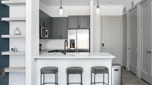 Cocina moderna con una isla central, electrodomésticos de acero inoxidable y taburetes de bar.
