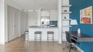A modern kitchen with white cabinets, a stainless steel refrigerator, and a bar area with two stools. - Landing | Stylish 1BD, Pool, Game Room (Austin)