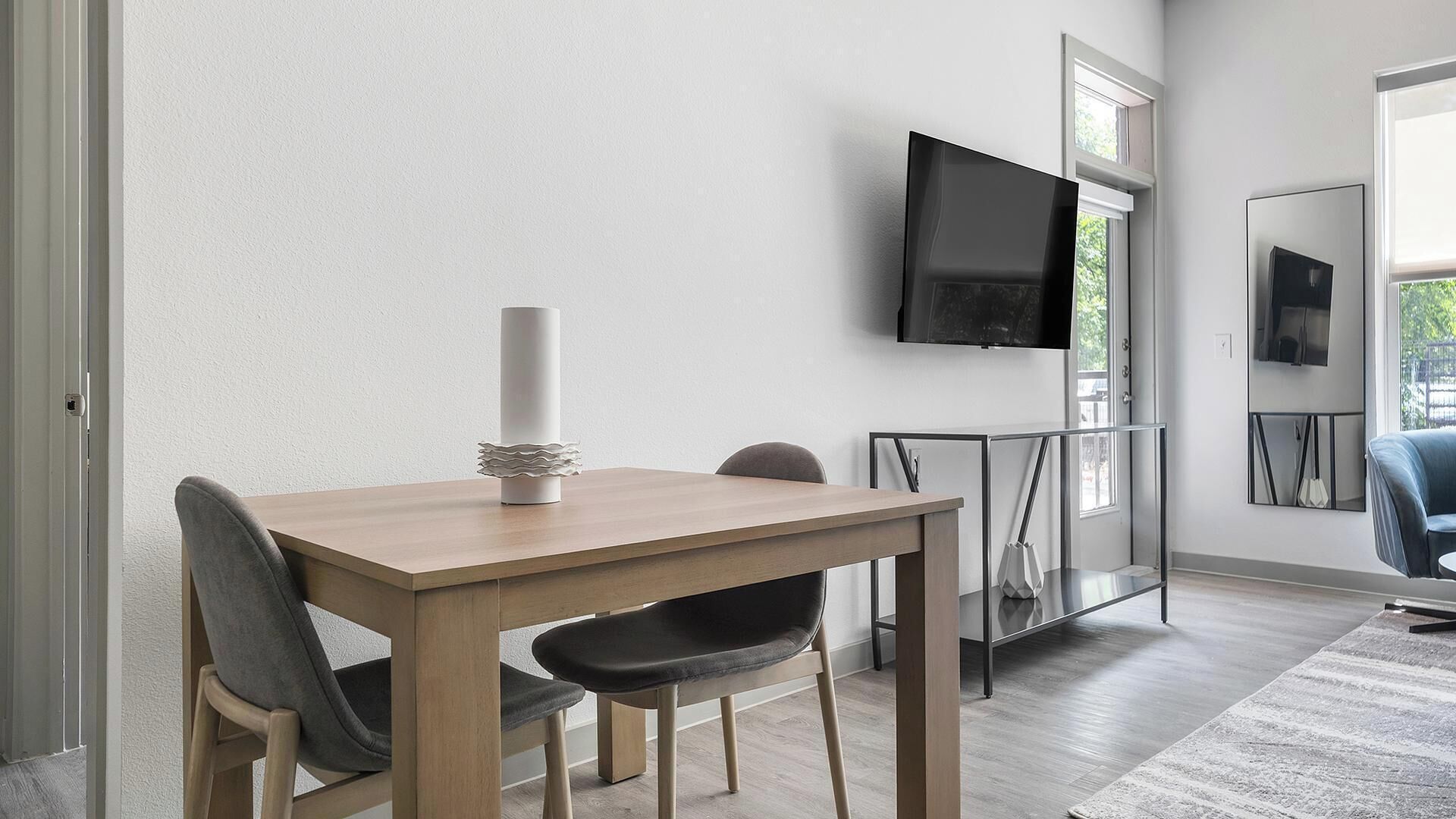 Un comedor moderno con una mesa de madera, dos sillas, una vela decorativa y un televisor montado en la pared.