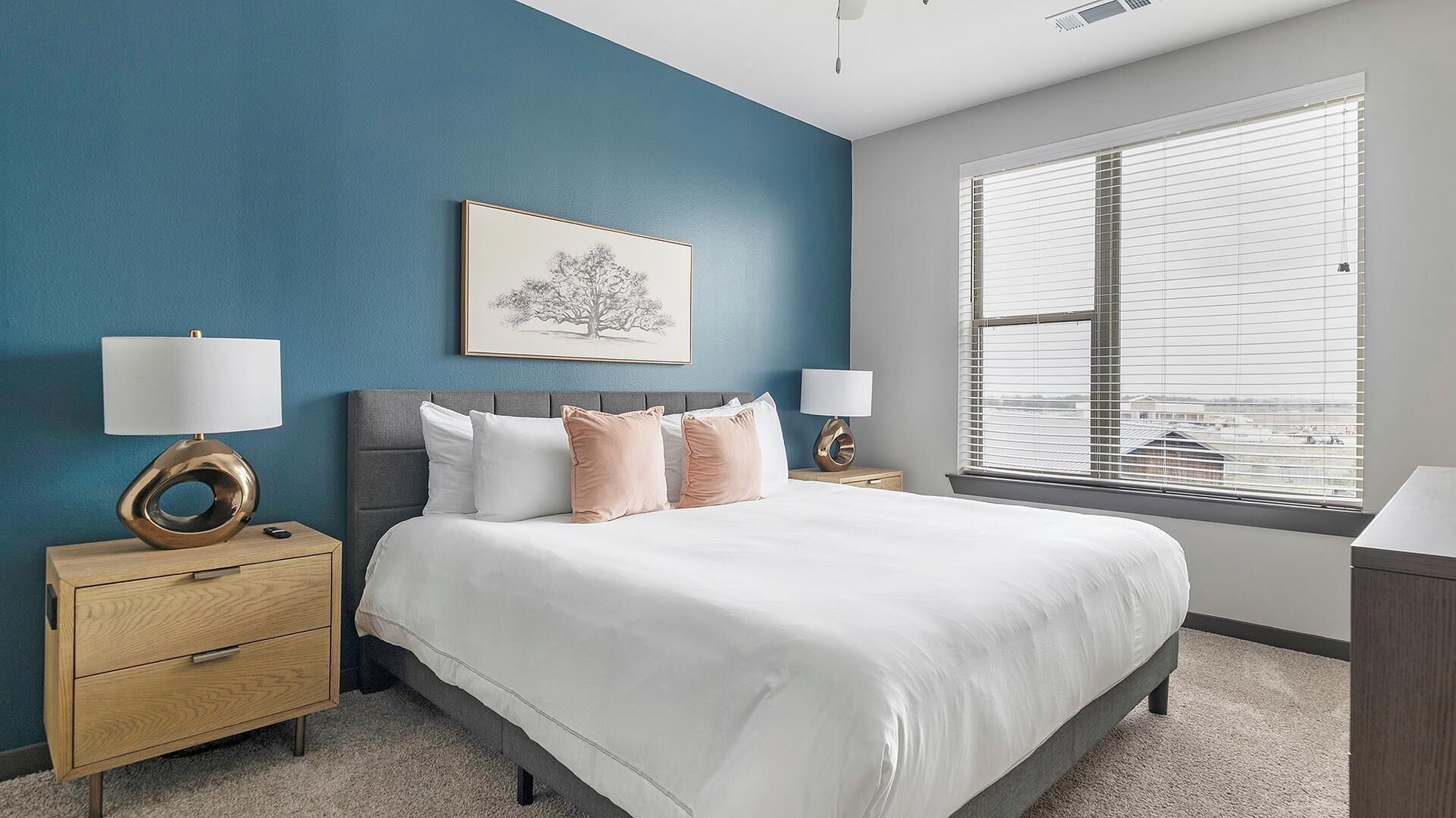 A bedroom with a bed, two bedside tables, a wall-mounted picture, and a window with blinds.