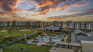 A modern apartment complex with multiple buildings, a central courtyard with a swimming pool, and a scenic sunset view. - Landing | Incredible 1BD, Clubhouse, Pool (Kyle)