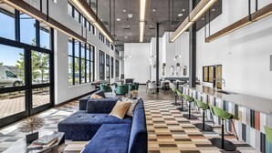 A spacious lobby with a blue sofa, a striped floor, and a bar area with green chairs. - Landing | Incredible 1BD, Clubhouse, Pool (Kyle)