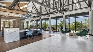 A spacious, modern interior with a large open area featuring a central island with bar stools, surrounded by green upholstered chairs. - Landing | Incredible 1BD, Clubhouse, Pool (Kyle)