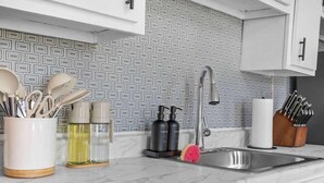 Uma cozinha com bancada de mármore, pia de aço inoxidável e painel de azulejos estampado.