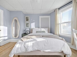 A bedroom with a bed, a nightstand, a mirror, and a window with curtains. - Subway Harvard MIT w Parking + Yard + Outdoor (Somerville)