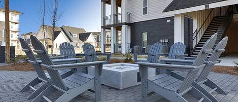 Eine Terrassenfläche mit Adirondack-Stühlen und einem zentralen Feuerkorb, umgeben von modernen Gebäuden.