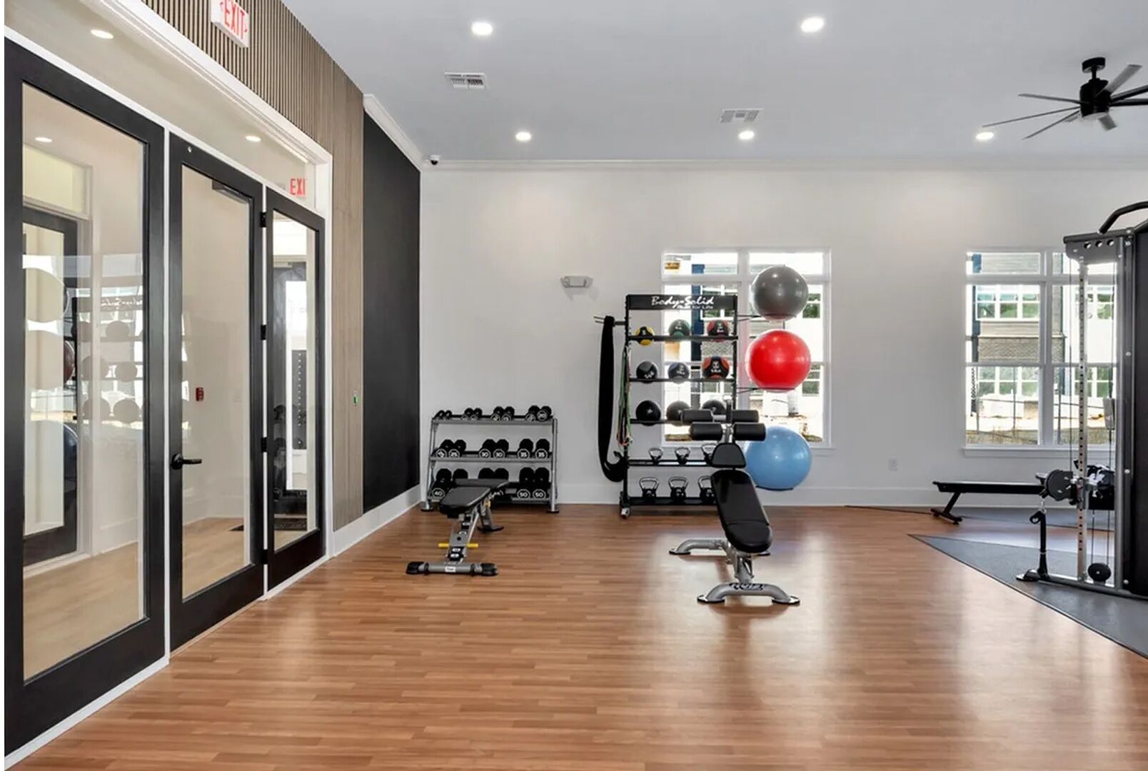 A modern gym with wooden floors, weightlifting equipment, and exercise balls.