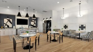 A modern kitchen with white cabinetry, a central island, and pendant lighting. There is a dining area with a round table and chairs, and a seating area with a checkered sofa and chairs. - Landing | Stunning 2BD, Pool, Yoga Studio (Athens)