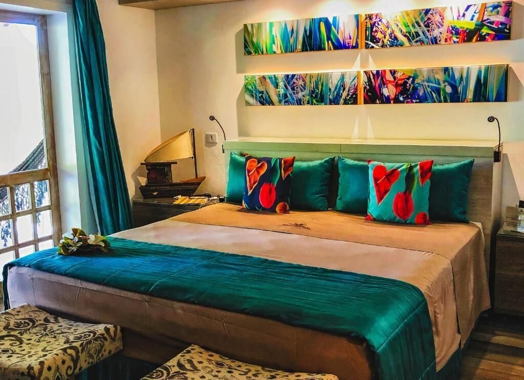 A hotel room with a large bed, a window with curtains, a nightstand with a lamp, and abstract artwork on the wall.