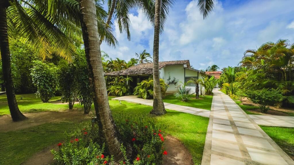 A house with a tiled roof, surrounded by lush greenery and palm trees.