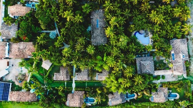 Luchtbeeld van een resort met meerdere bungalowachtige accommodaties, omgeven door weelderige palmbomen en een zwembad.