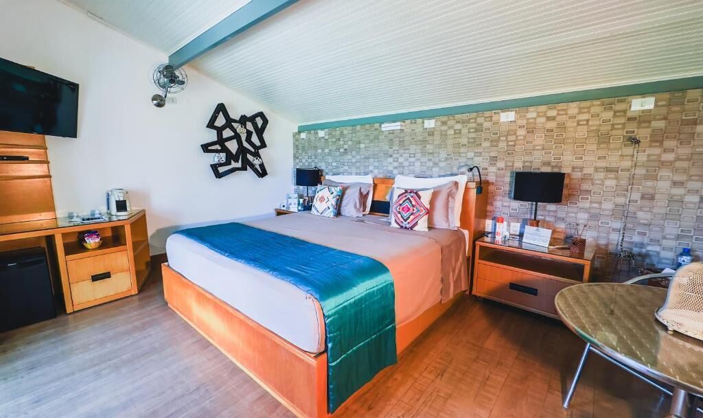 Quarto de hotel moderno com uma cama grande, mesas de cabeceira, televisão e uma pequena área de trabalho.