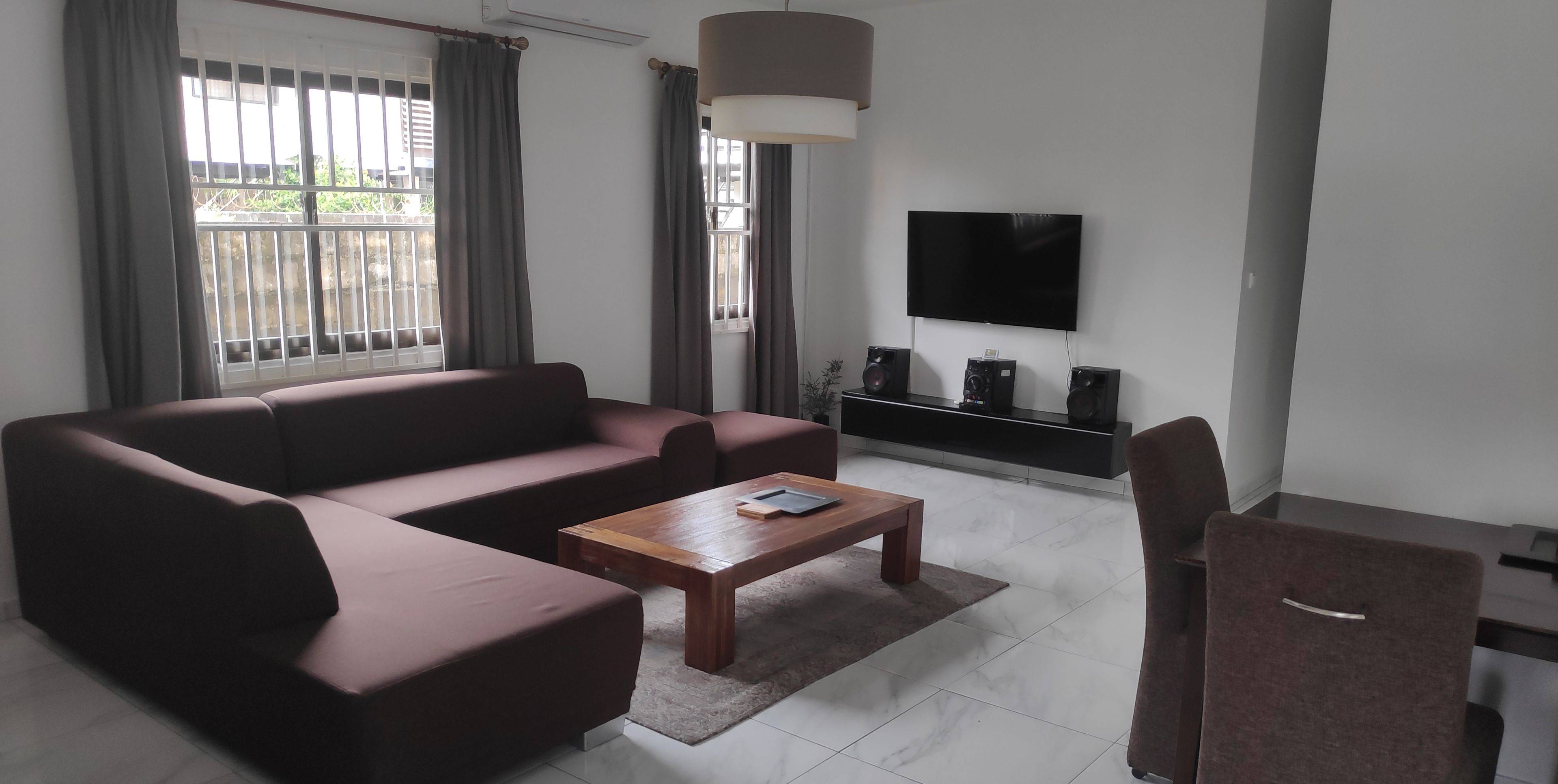 A modern living room with a sectional sofa, a wooden coffee table, a TV mounted on the wall, and a small cabinet.