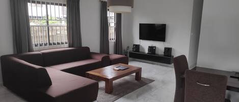 Una sala de estar moderna con un sofá seccional, una mesa de centro de madera, un televisor montado en la pared y un mueble bajo.