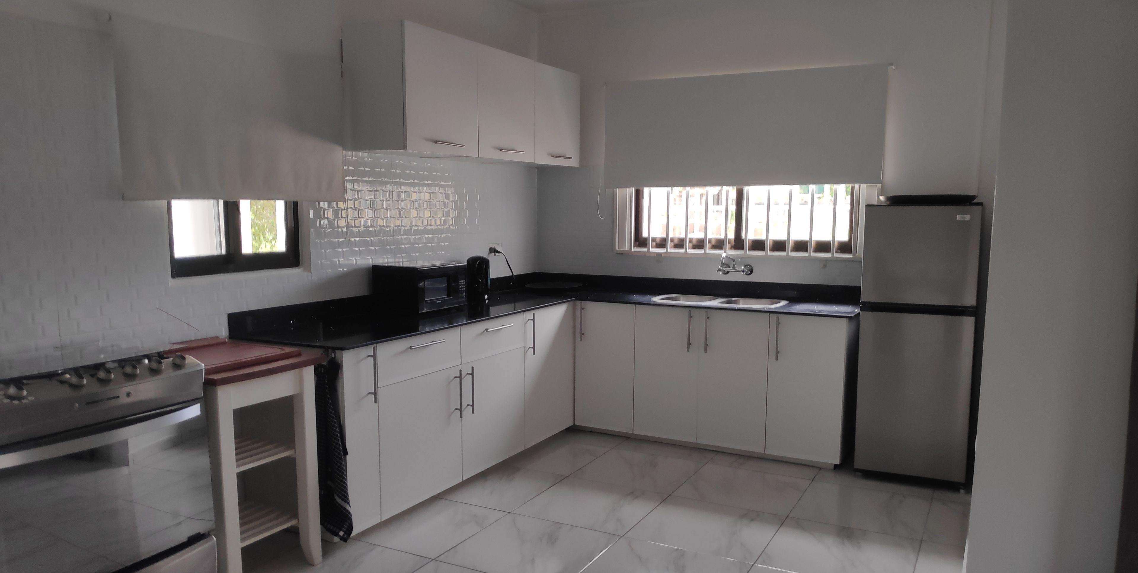 Una cocina moderna con armarios blancos, encimera negra, un lavamanos y un refrigerador.